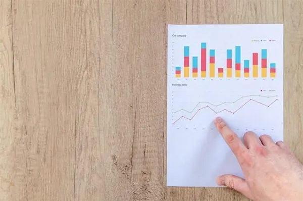 A person pointing to graphs on a piece of paper, on a wooden surface