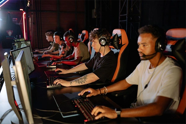 Gamers wearing headsets compete at a row of gaming PCs in a dimly lit esports arena